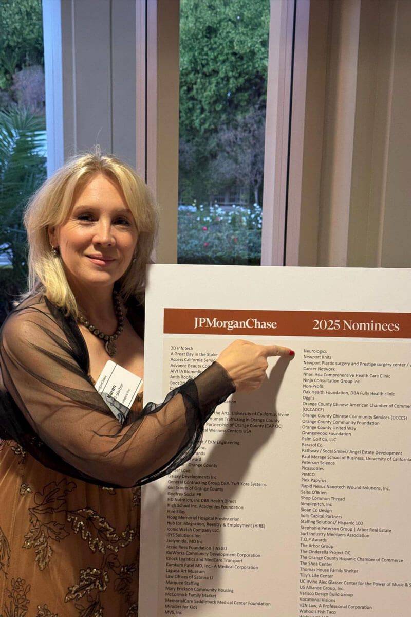Woman in a tan floral dress pointing at a large JP Morgan Chase 2025 nominees board near tall windows.