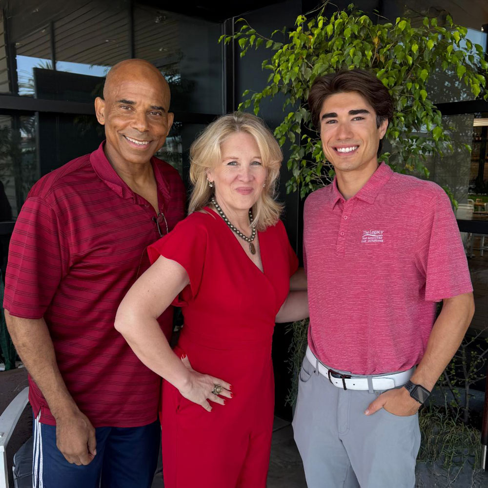Three people smile together outdoors, two men and one woman, all dressed in red and posing for a friendly photo.
