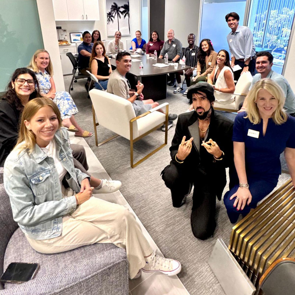 A large group of people sit together in a conference room smiling for a group photo during a meeting or event.
