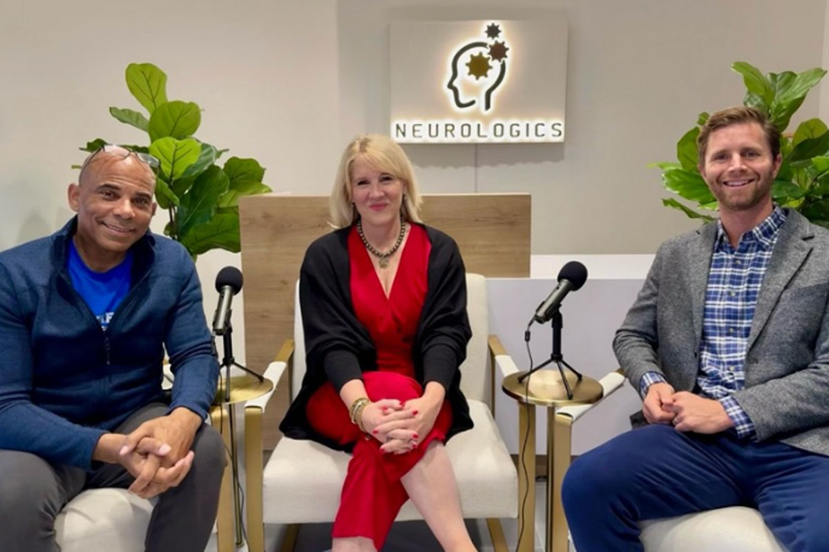 Three people sit together in a studio setting with microphones, smiling in front of a Neurologics sign.
