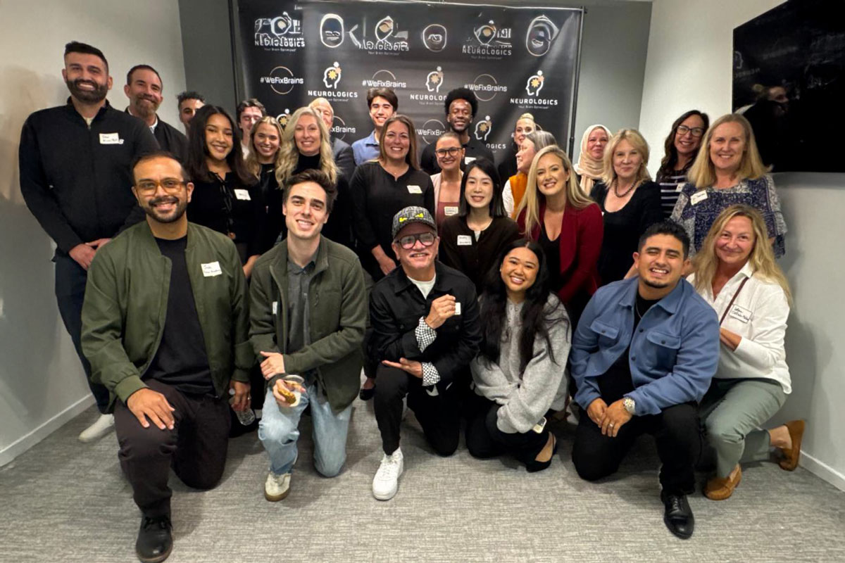 A large group of attendees pose together in front of a Neurologics backdrop at an event.