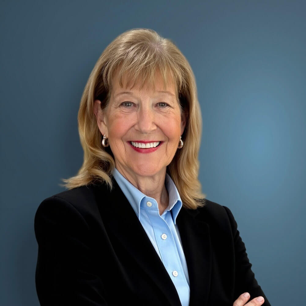 A professional headshot of a smiling woman in business attire against a blue studio background.