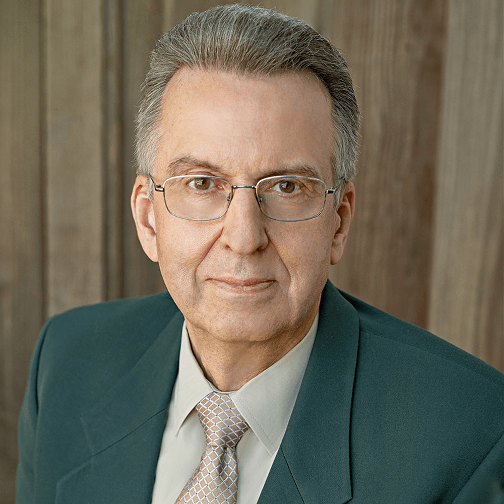 march_newsletter_2026_1 A professional headshot of an older man wearing glasses and a suit, posed against a neutral wood background.