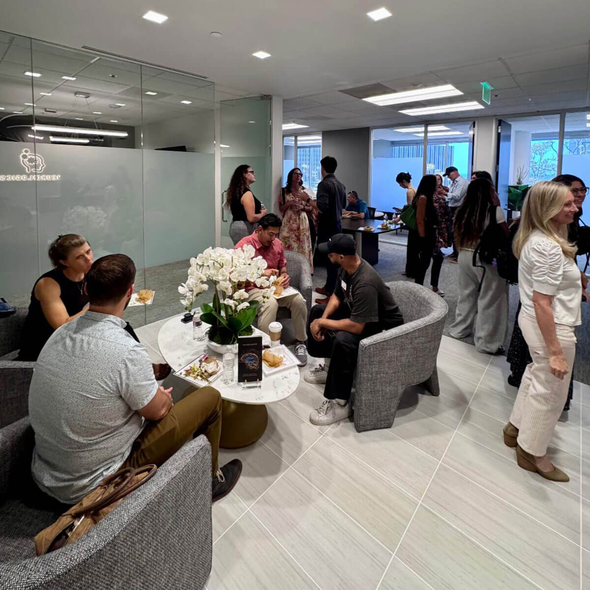 july_newsletter_2026_5 Attendees mingle, chat, and enjoy a catered lunch in a modern Neurologics office lounge area during a networking event.